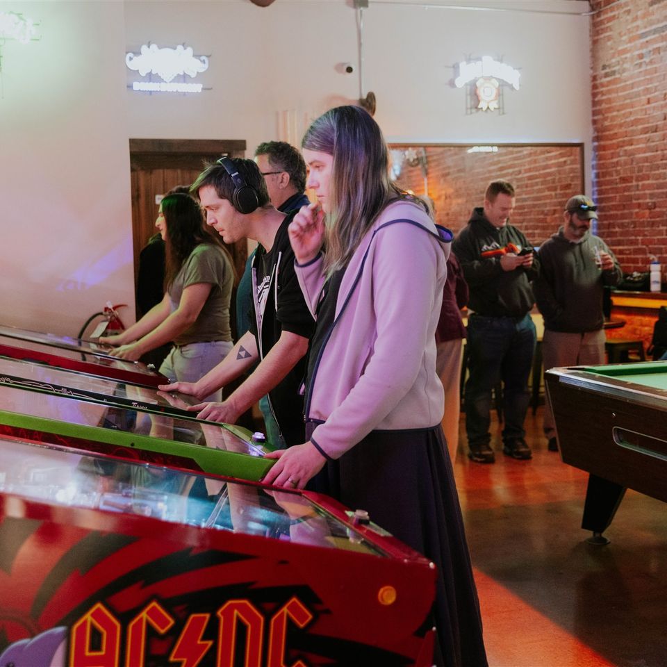 Group of people playing pinball machines and pool