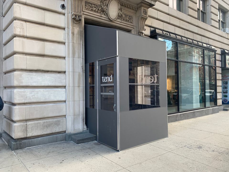 Grey aluminum framed vestibule with clear panels and white vinyl door lettering at the entrance of a limestone building