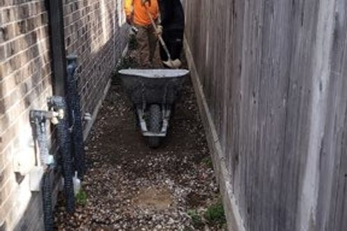 Crew uses wheelbarrow to spread gravel sub‑base for new side walkway in Spring, TX