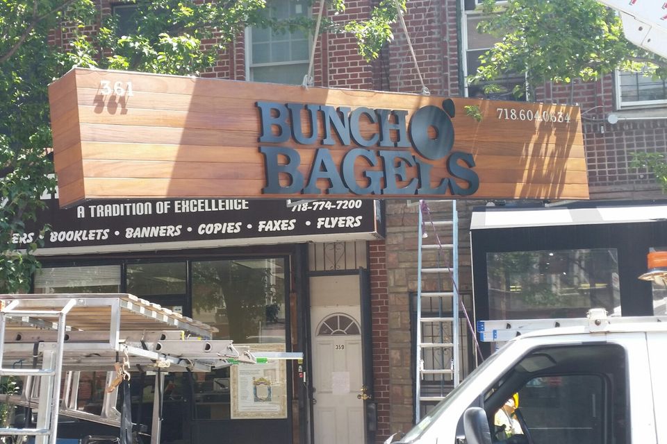 Wood-clad storefront sign with dimensional lettering above a bagel shop entrance