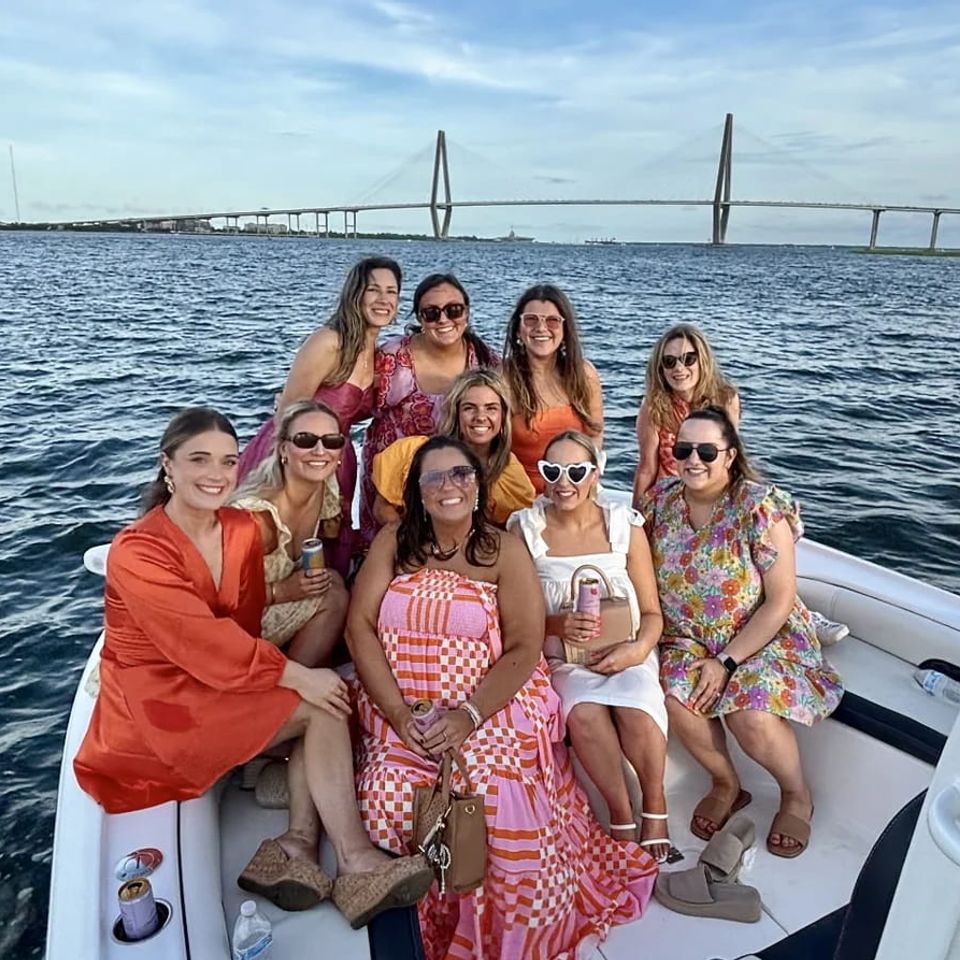 Group of women celebrating a bachelorette party on a Charleston boat tour with the Ravenel Bridge in the background on a sunny evening
