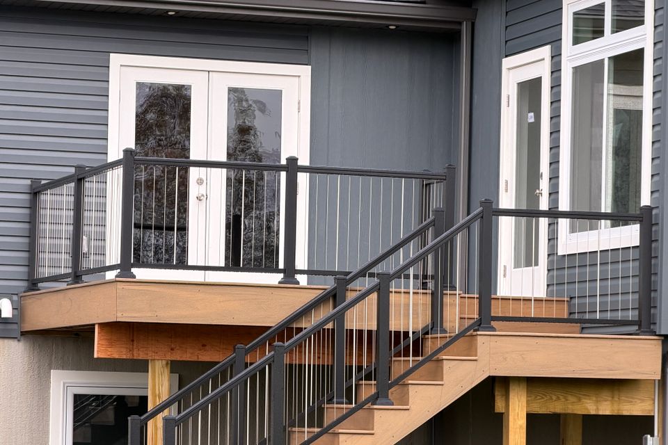 Custom wood deck featuring black metal railings, stair access, and entry doors attached to a residential home.