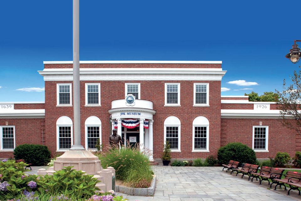 Brick building with white accents.  Red white and blue bunting.  Bronze statue of JFK