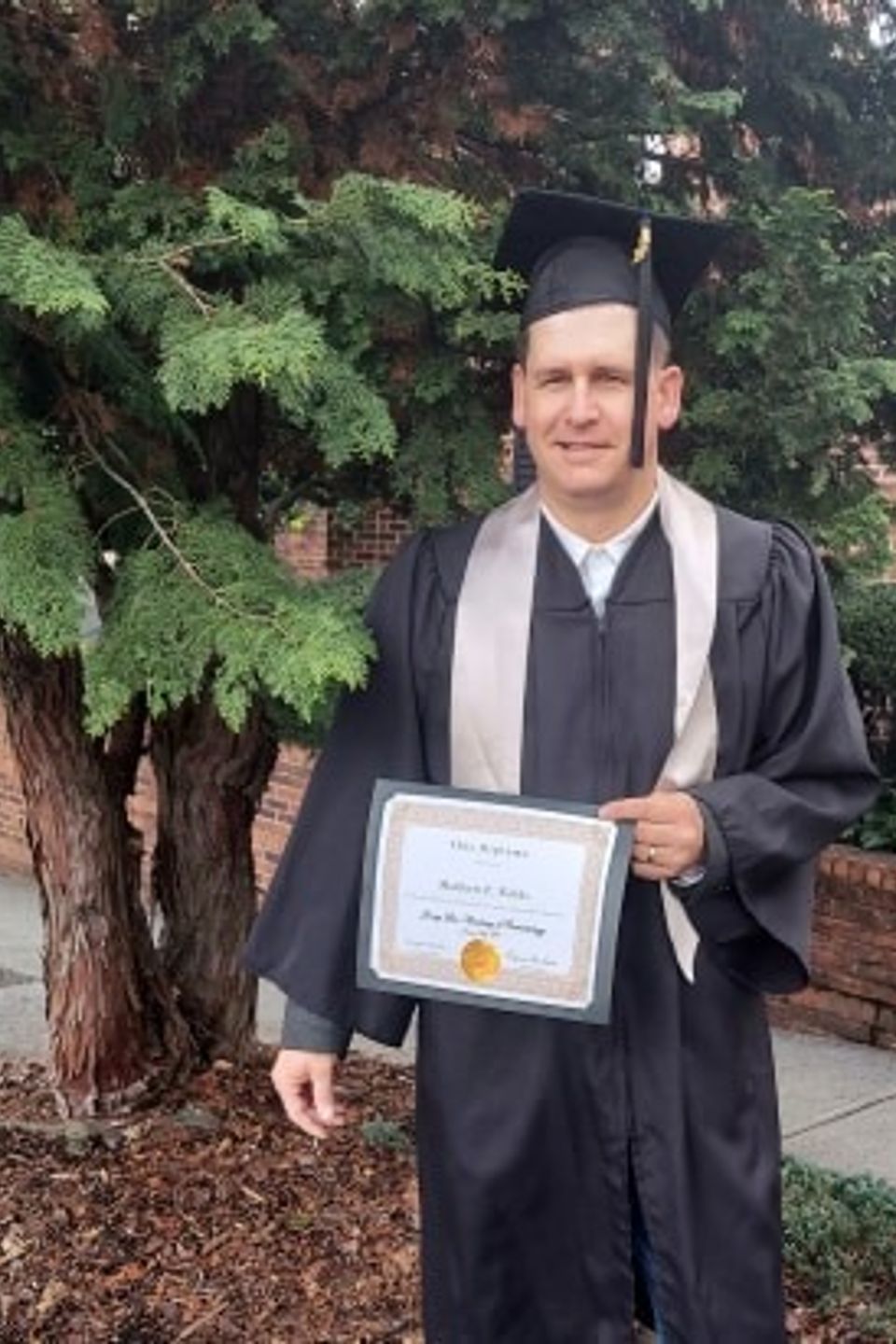 Barbering program graduate holding certificate outdoors
