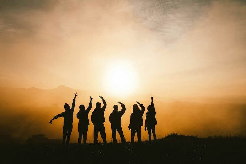 Sihouettes of a group of 6 people at sunset all cheering