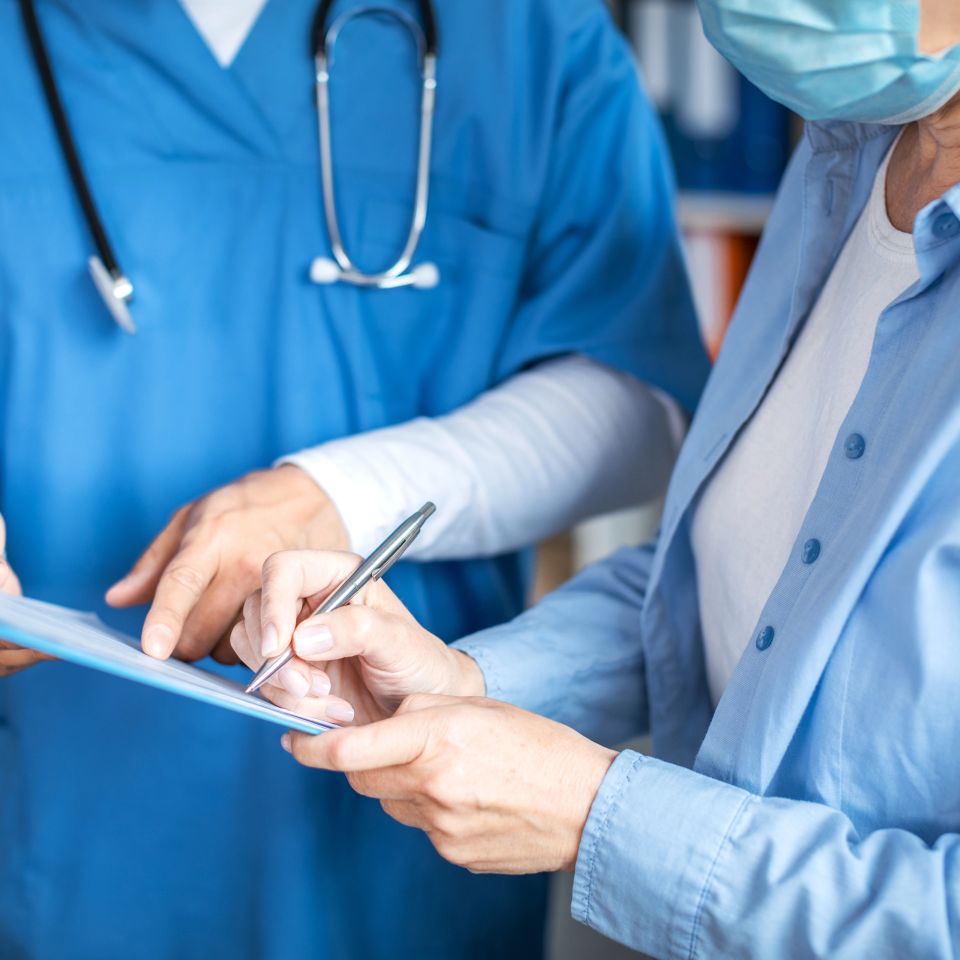 Smiling adult man doctor and elderly lady patient signing documents in clinic office
