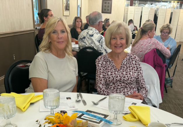 Two women seated at a table during the Mahoning Valley September meeting with other attendees in the background.