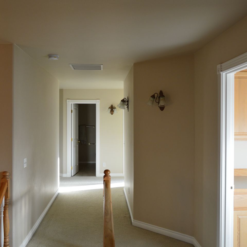 Upstairs hallway with wall sconces, carpet, and open bedroom doorway in a finished custom home