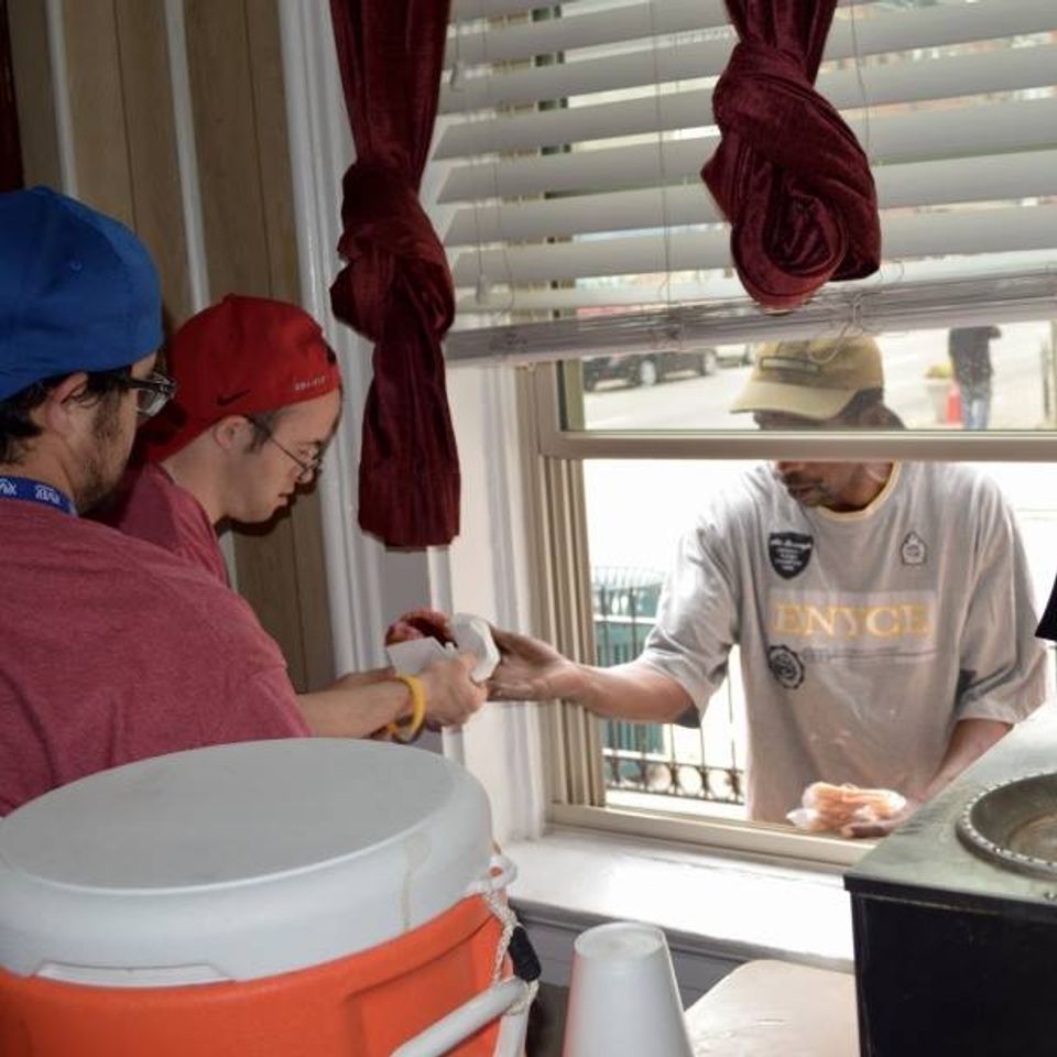“Volunteers handing food to a man through a service window at the Catholic Worker House.”