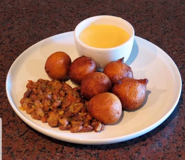 Golden fried puff puff dough balls with seasoned beans and a cup of dipping sauce