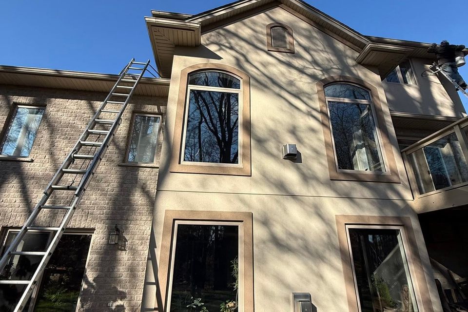 Technician on ladder cleaning gutters on two-storey stucco and brick home in Tillsonburg Ontario