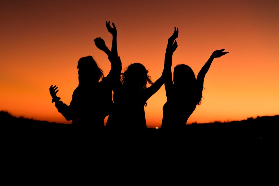 3 people with their arms in the air featuring just their silhouettes at a sunset 