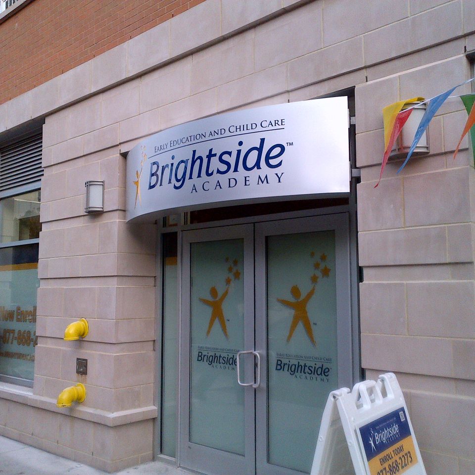 Curved white illuminated cabinet sign with a logo mounted over a double-door entrance