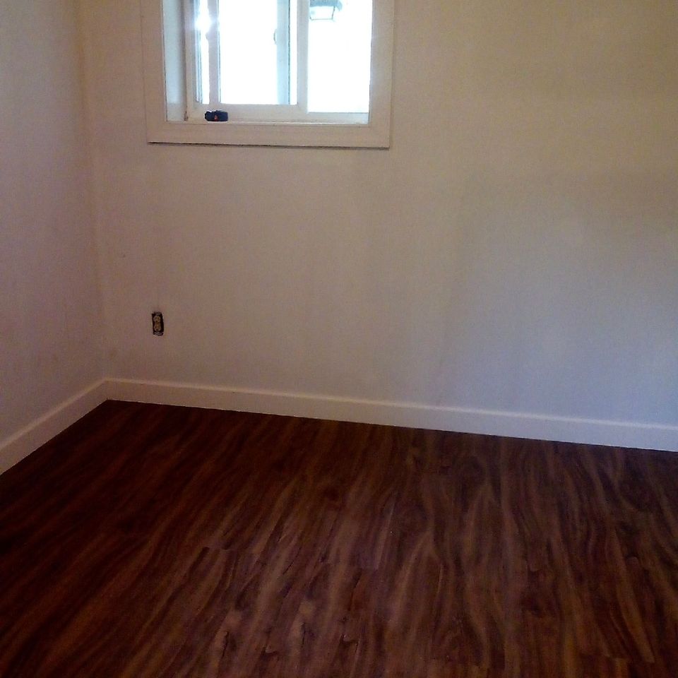 Empty bedroom with fresh white walls baseboard trim and new laminate flooring installation