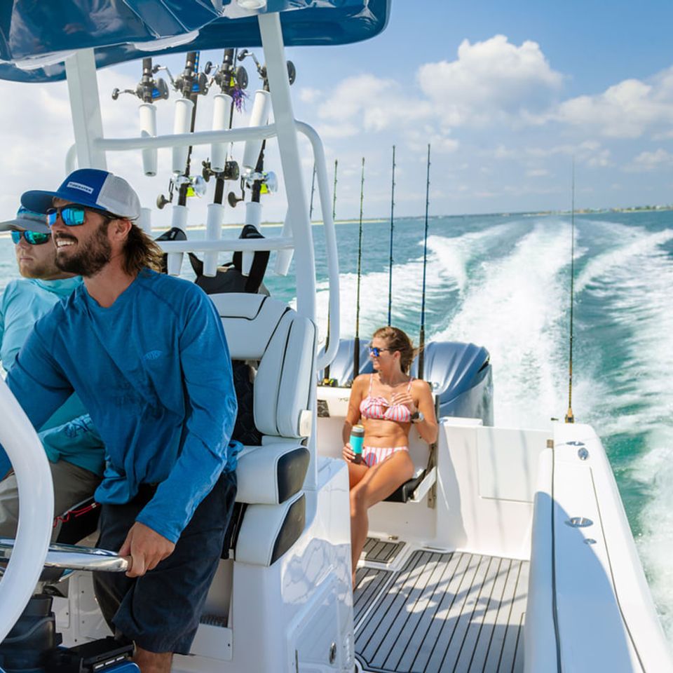 Two Charleston fishing charter captains driving a center console boat with a guest relaxing in the back on a sunny day