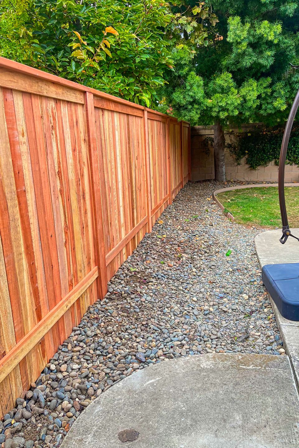 Freshly built wooden fence beside curved river rock landscaping and concrete patio