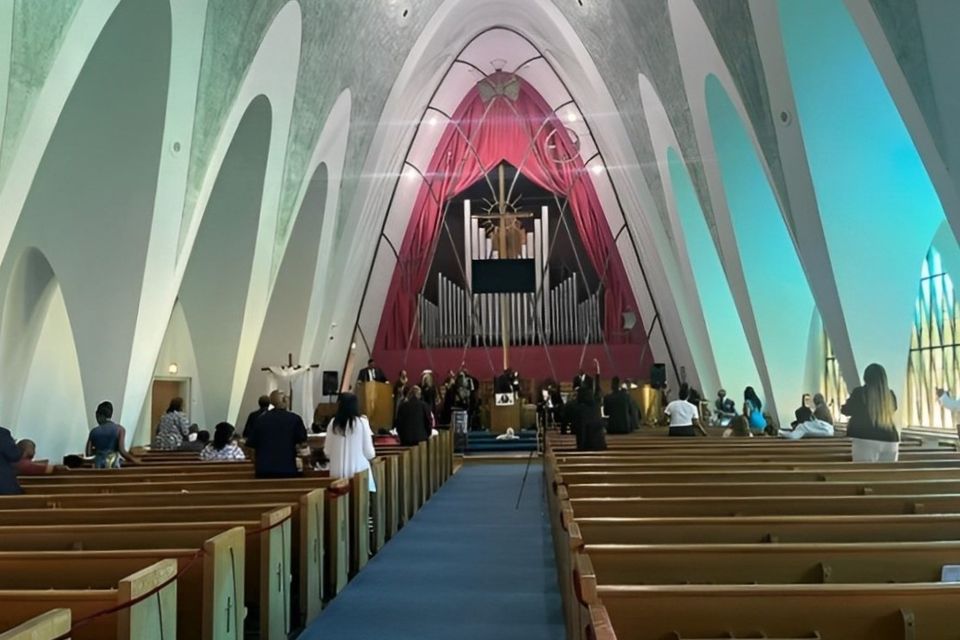 Interior view of Grace Evangelistic Temple Church showing worshippers seated in wooden pews facing the altar, cross, and choir area within the church’s high-arched sanctuary.