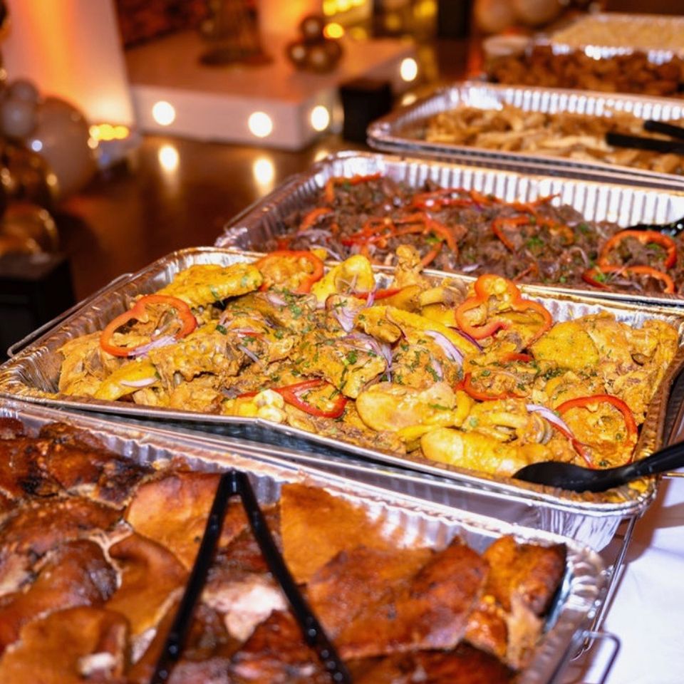 Catered buffet trays of roast pork, chicken, and beef served beside gold balloon decor at a Hamptons NY event