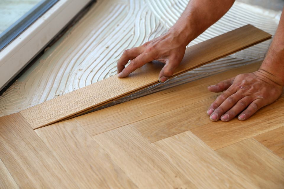 Worker laying oak parquet planks into adhesive during a wood flooring installation
