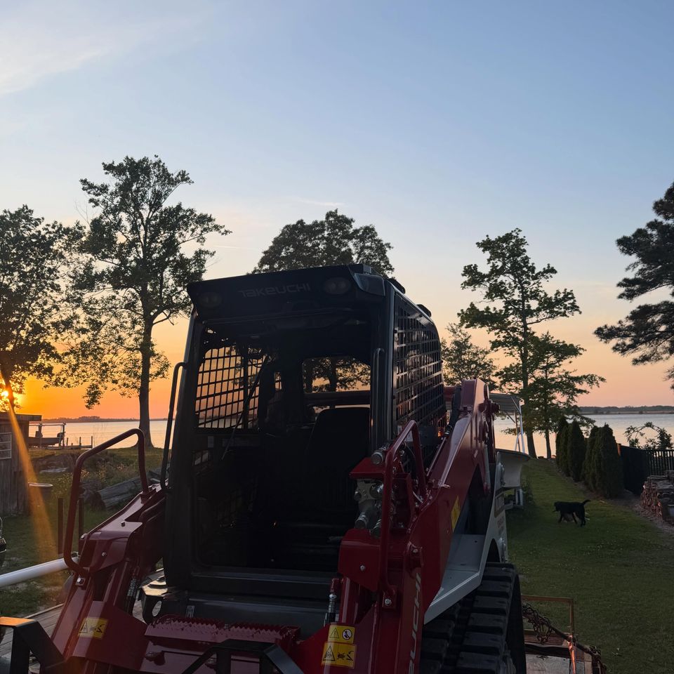 Takeuchi track loader with tinted cab glass on a trailer at sunset by the water