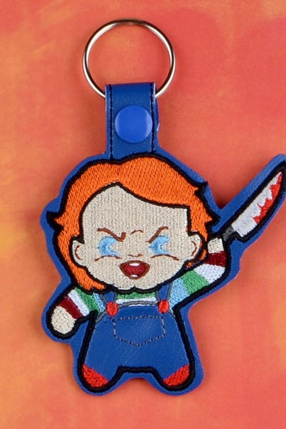 Custom embroidered horror doll keychain with orange hair, overalls, and a stitched knife detail.