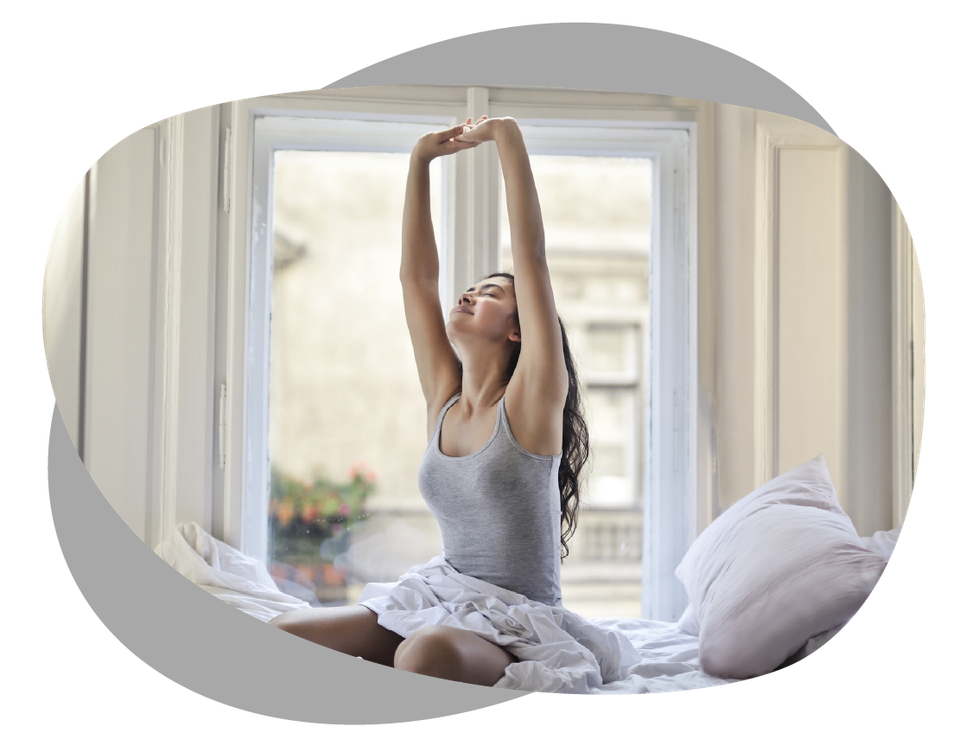 Woman stretching in bed after waking, representing renewed energy and vitality after mobile IV therapy
