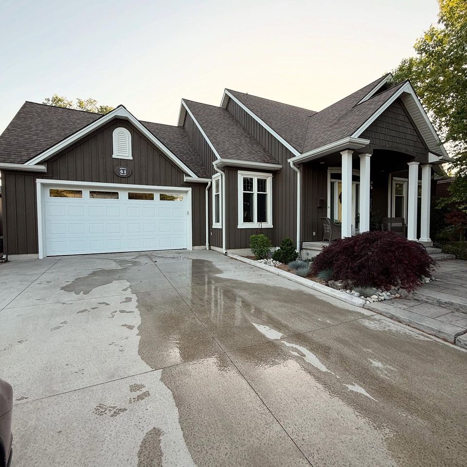 Wet concrete driveway after a pressure washing in front of a brown board-and-batten home in Tillsonburg Ontario