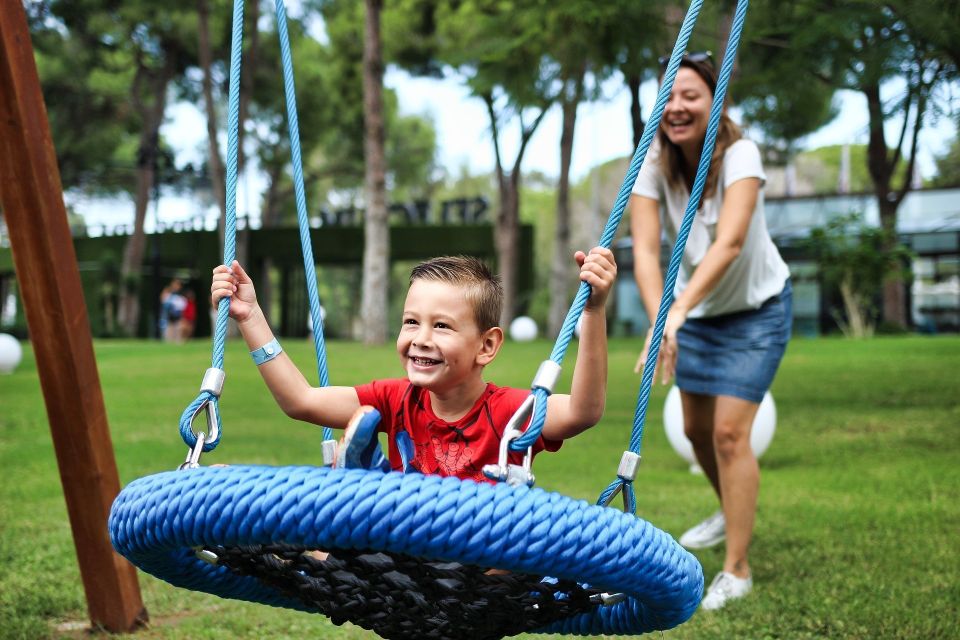 Smiling boy on a blue rope swing while an adult pushes him during outdoor playtime in Palmdale CA