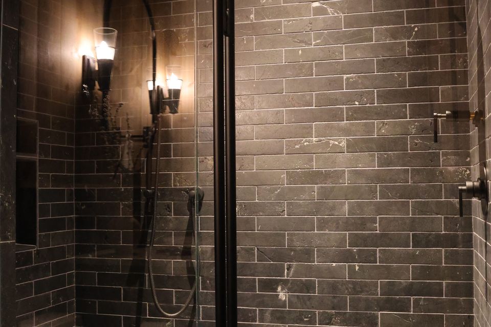Custom-built luxury shower with dark gray stacked bond tile walls, a built-in bench, and black matte fixtures, showcasing high-quality tile installation and modern bathroom design by Luxe Design Granite and Tile.
