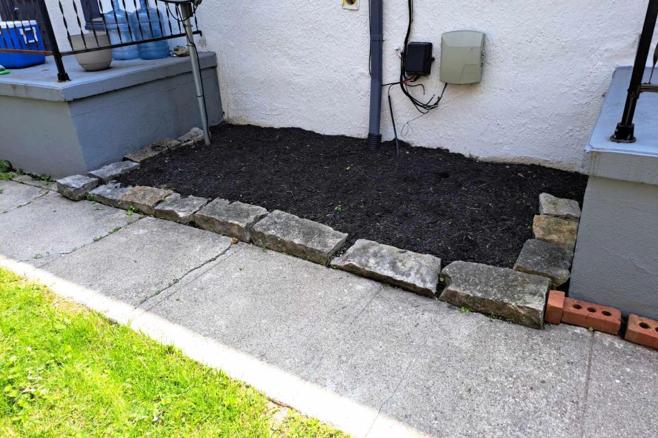 Small landscape bed filled with fresh black mulch and bordered with decorative stone edging.