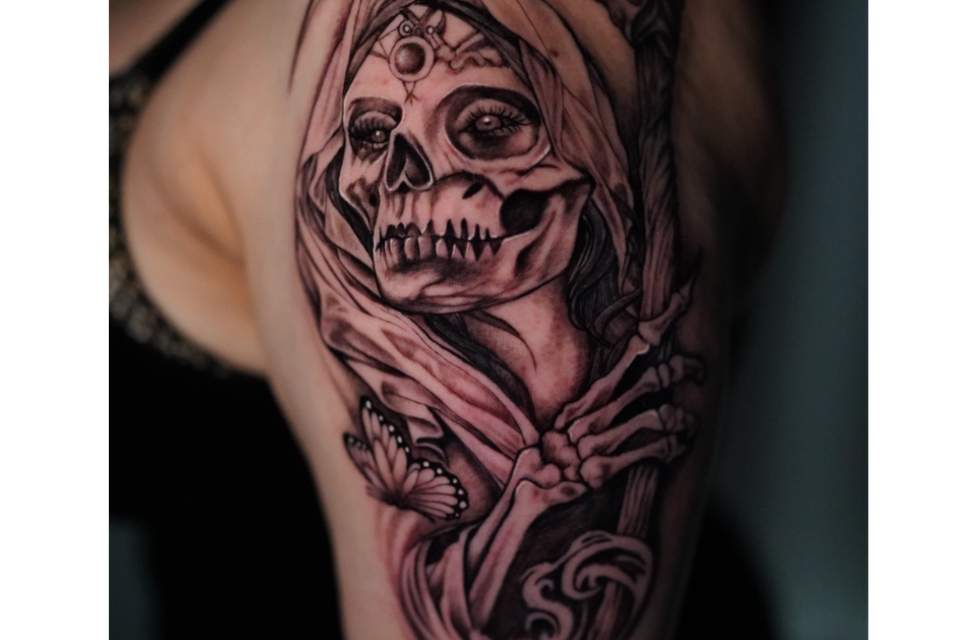 Image of a royal tattoo as a skeleton adorned with head wrapping and sceptor and a butterfly