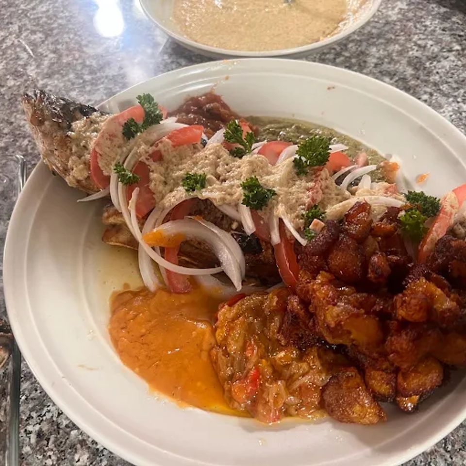 Grilled fish topped with onion and tomato served with fried plantains in sauce at a Los Angeles Cameroonian kitchen