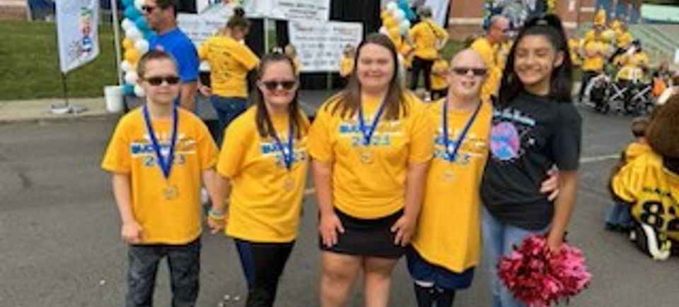 Group of young Buddy Walk participants wearing medals and posing with a cheerleader.