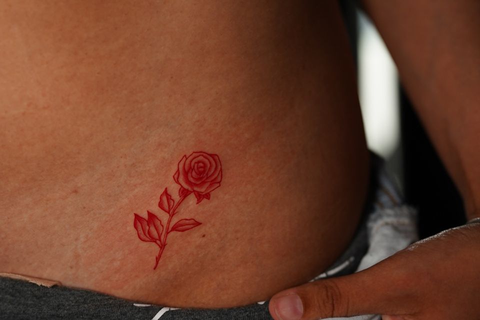Image of a red rose with stem tattoo on a womans left front just above her thigh