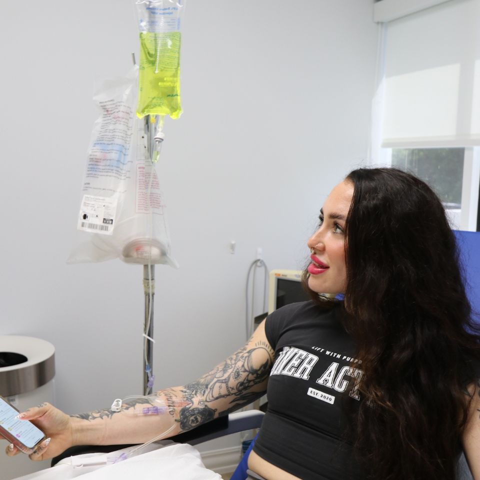 Smiling woman holding her phone while receiving a vitamin IV drip in Palm Beach County FL