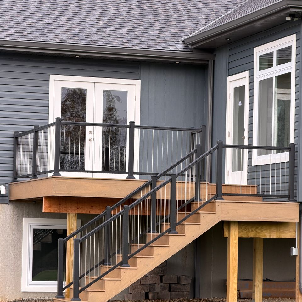 Custom wood deck featuring black metal railings, stair access, and entry doors attached to a residential home.