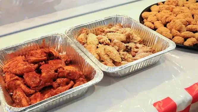 Catering trays filled with sauced wings, seasoned wings, and breaded appetizer bites.