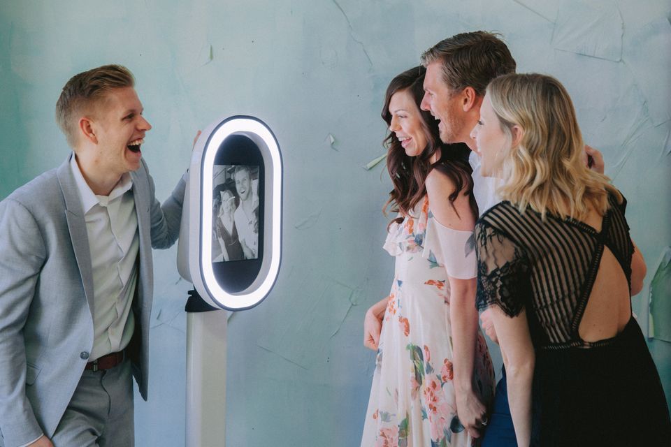 Group of friends laughing and posing together in front of a digital photo booth indoors