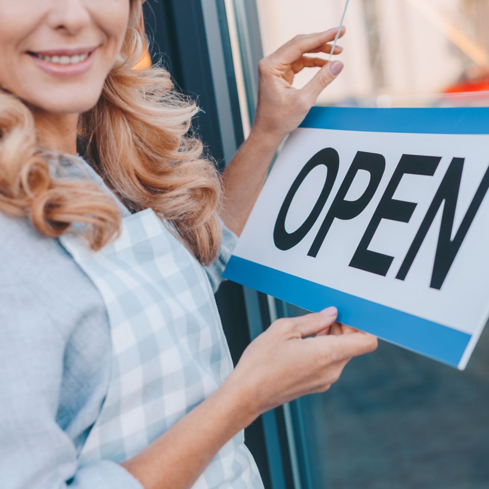 Cropped shot of smiling cafe owner in apron holding sign open 