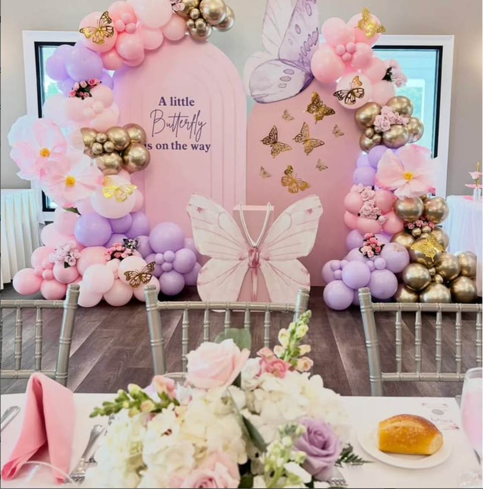 Elegant butterfly-themed baby shower backdrop with pink and lavender balloon garlands, gold accents, and floral decorations by Aldys Events