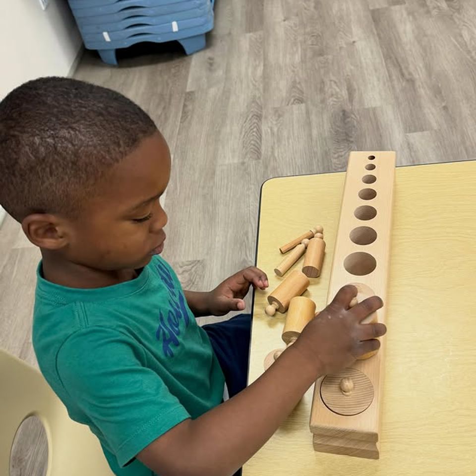 Preschool boy working with wooden Montessori knobbed cylinders at a classroom table in Palmdale CA