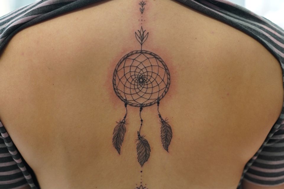 Image of a woman's back with a dream catcher tattoo in black and grey