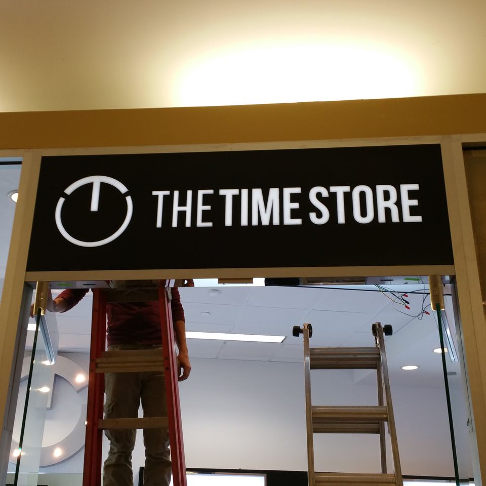 Installer on a ladder mounting an illuminated stencil cut sign above a storefront entrance