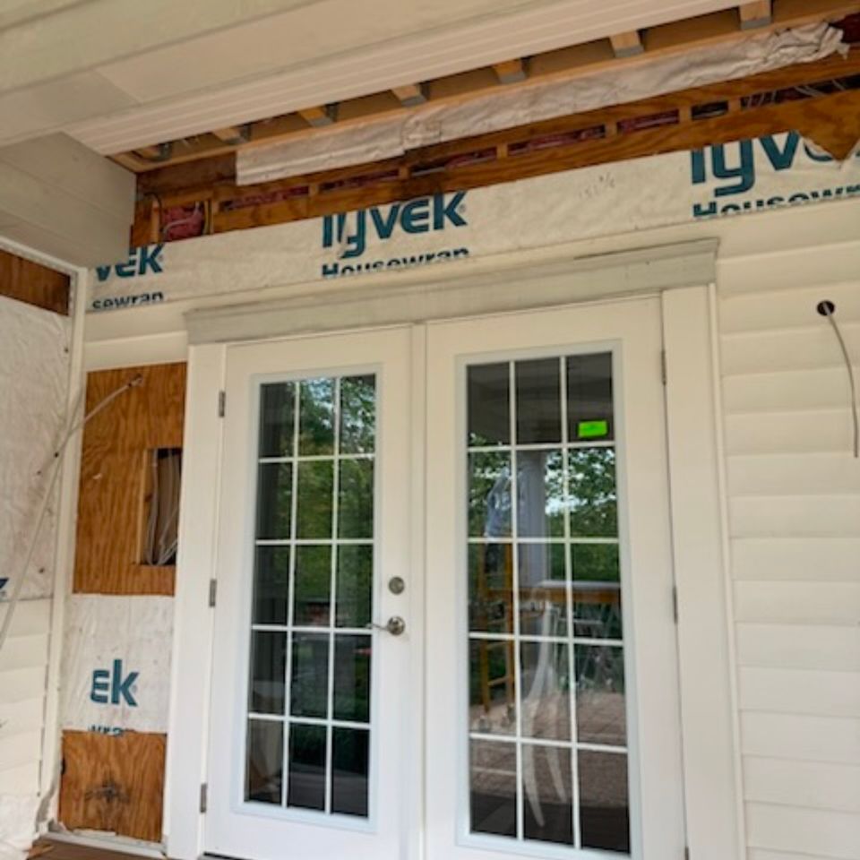 White French patio doors with Tyvek housewrap and exposed framing during a covered porch renovation