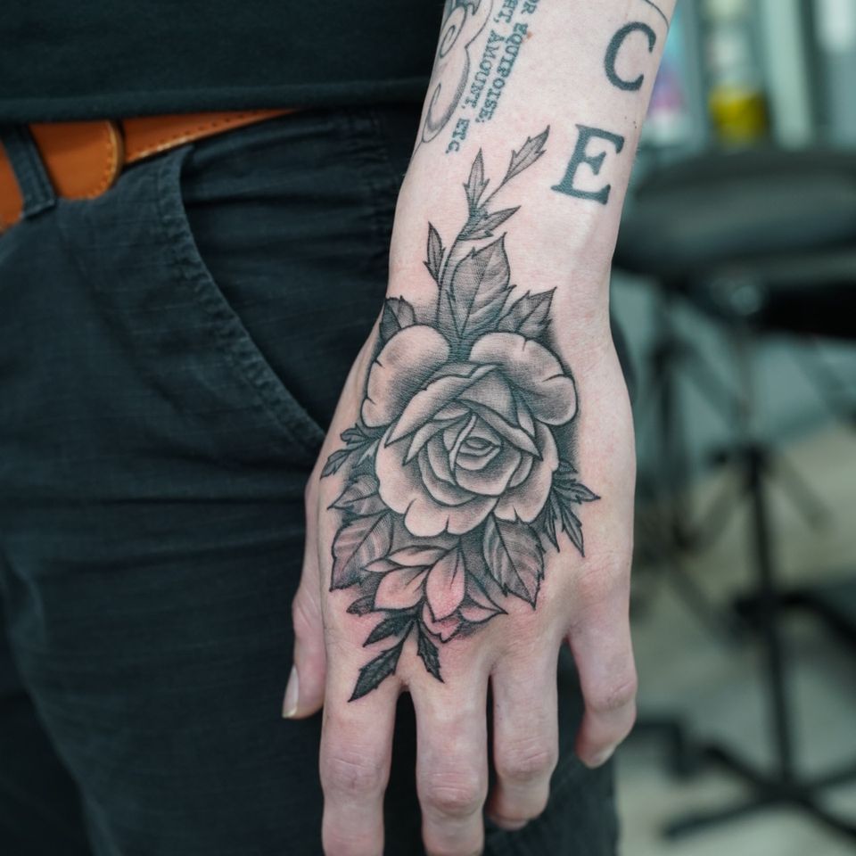 Image of a rose tattoo on a mans hand in black and grey
