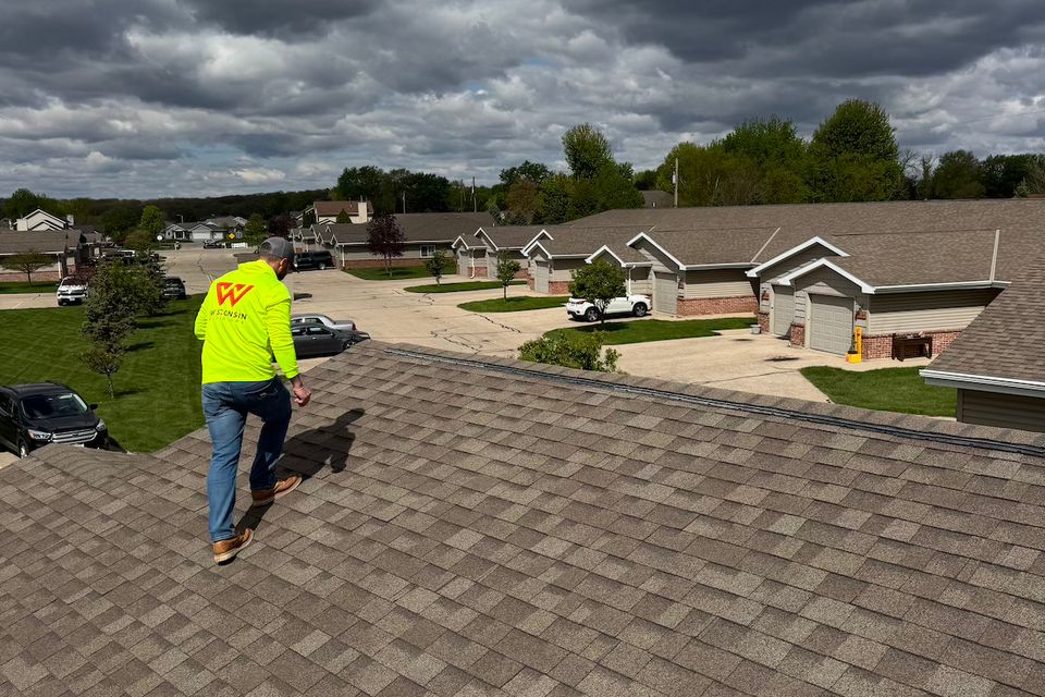 Roofing contractor inspecting apartment roof in Wisconsin with clipboard