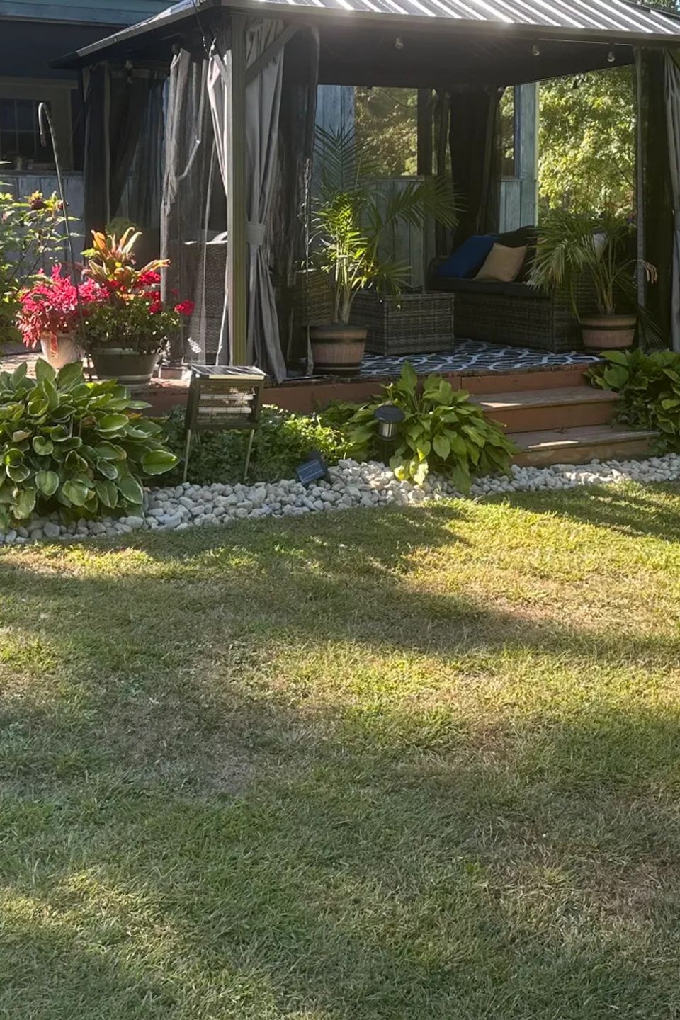 Residential backyard featuring a gazebo, decorative stone borders, flowering plants, hostas, and professionally maintained landscaping by R.E.P. Companies.
