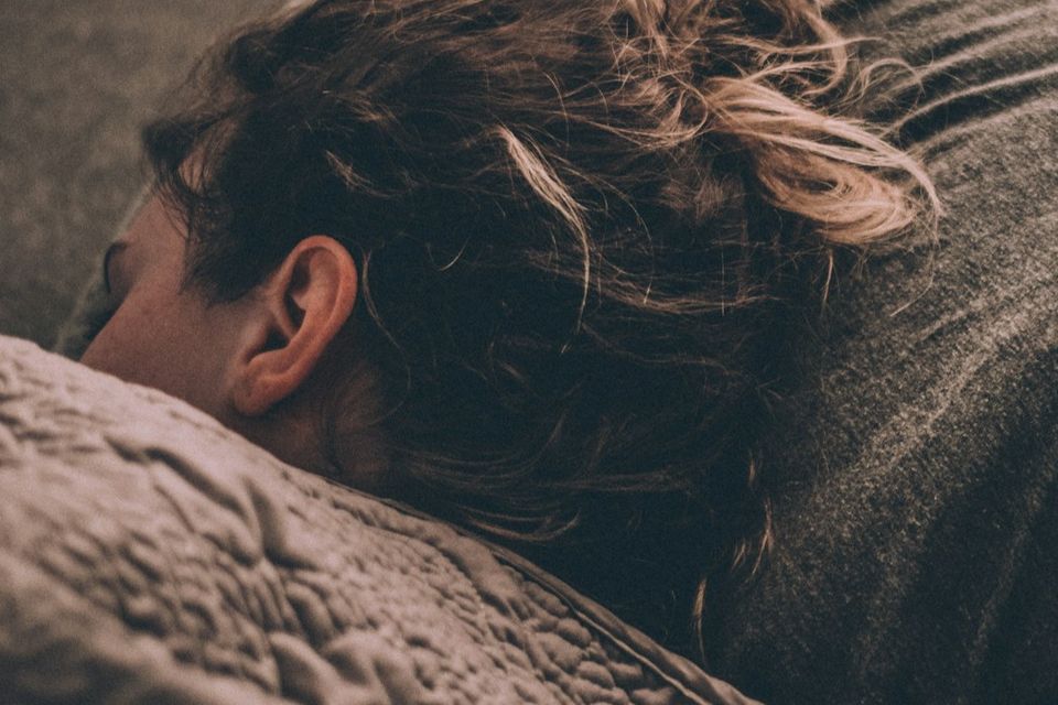 Woman sleeping in bed with part of her face visible under the covers, representing rest, fatigue, sleep quality, and low energy