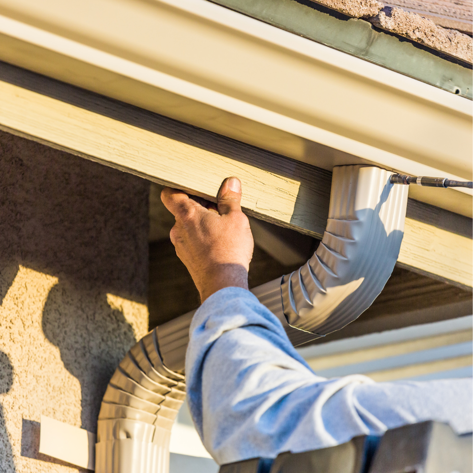 Technician installing a residential gutter system along the roofline of a home.