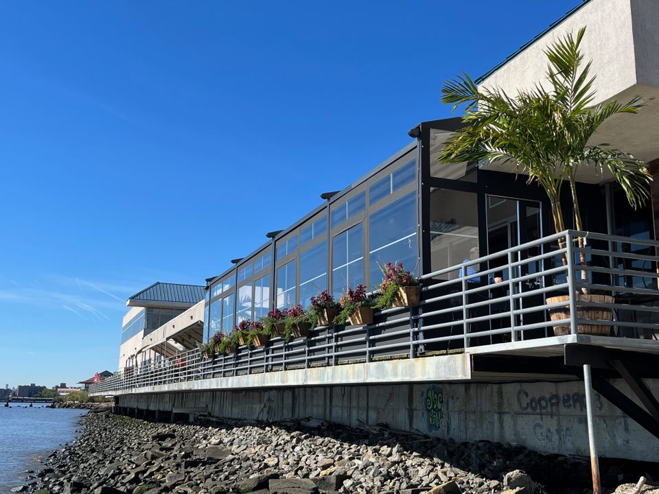 Glass paneled winter enclosure with a black aluminum frame running the length of a waterfront restaurant deck